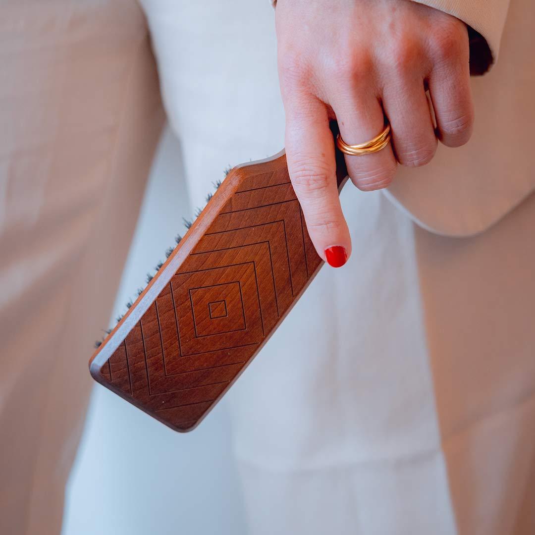Hand holding a natural hair brush with wild boar bristles, perfect for detangling and improving hair health.