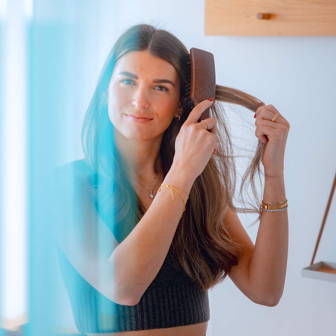 Woman using a natural hair brush on her long hair, showcasing the benefits of a wild boar bristle hairbrush.