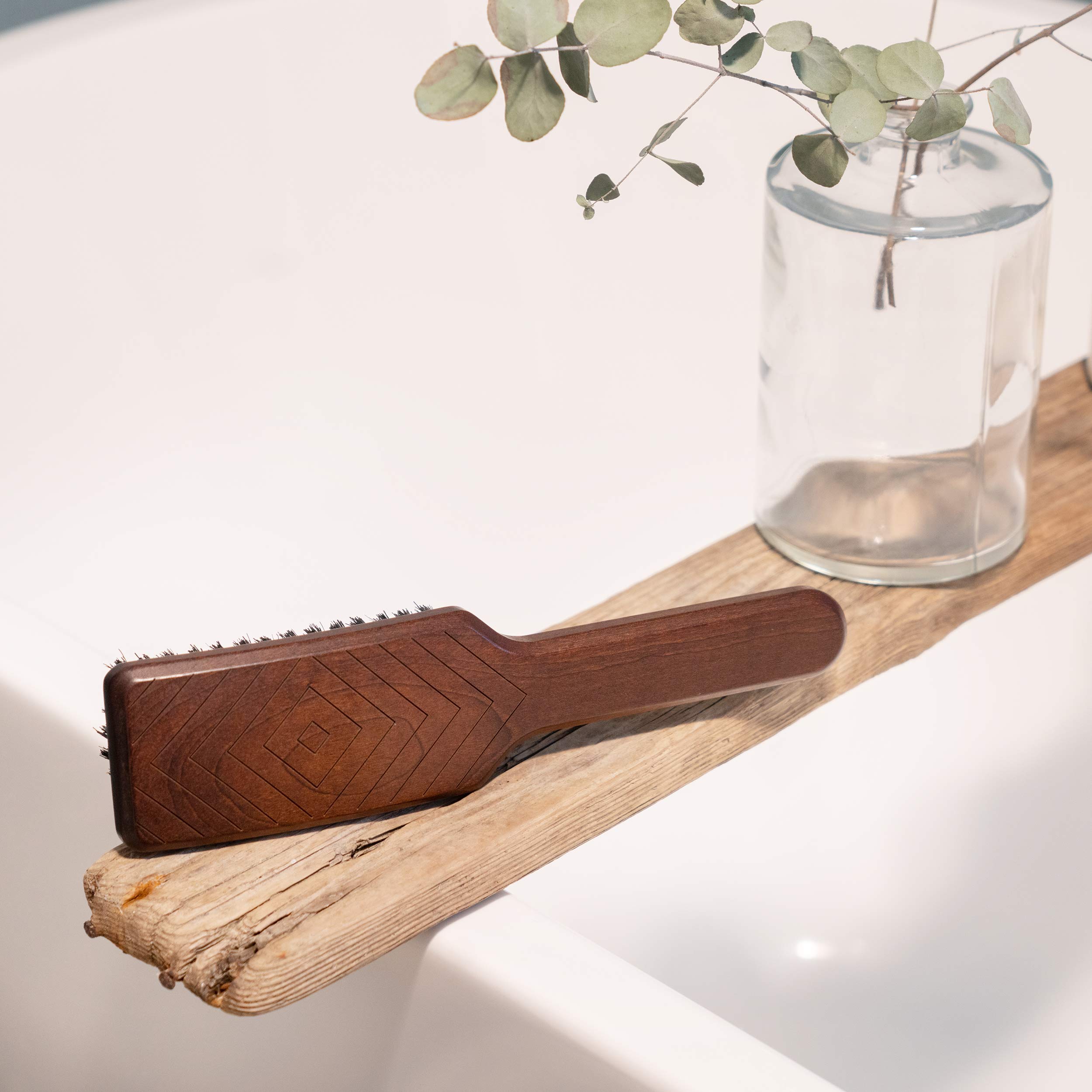 Natural hair brush with wild boar bristles displayed on a wooden ledge next to a glass vase and greenery.